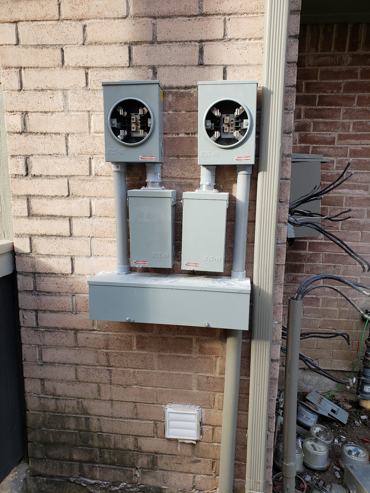 Side-by-side Eaton meter sockets and trough on a light brick wall